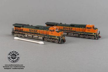 Two detailed BNSF model trains on a gray surface with a cotton swab for scale.
