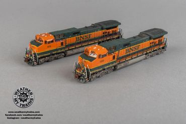 Two detailed BNSF model trains displayed on a gray surface.