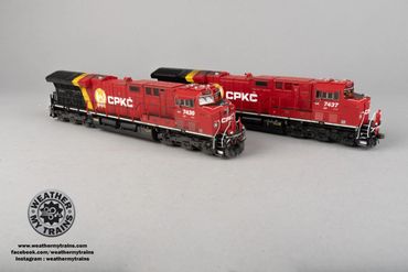 Two detailed red CPKC model trains on a plain surface.