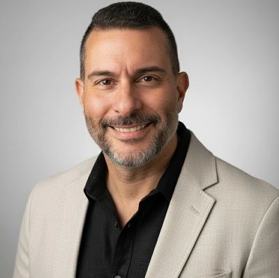 Confident man in beige blazer smiling against a neutral background.
