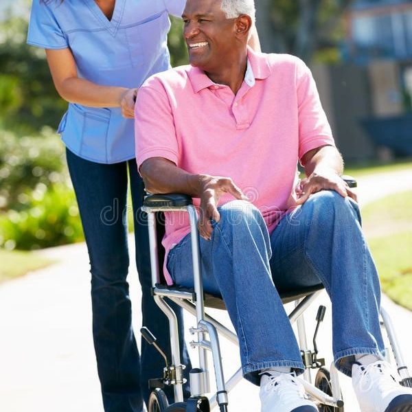 Smiling man in wheelchair being pushed by caregiver outdoors.
