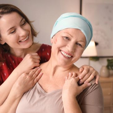 A woman with a headscarf and lipstick marks smiles with a supportive friend behind her.