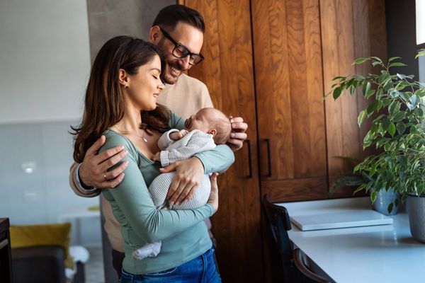 Portrait of young happy man and woman holding newborn cute babe dressed in white unisex clothing