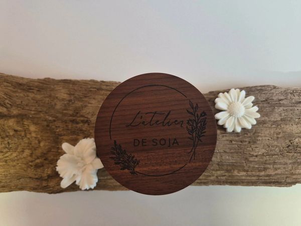 Wooden lid with 'L'atelier DE SOJA' on rustic wood and white flowers.