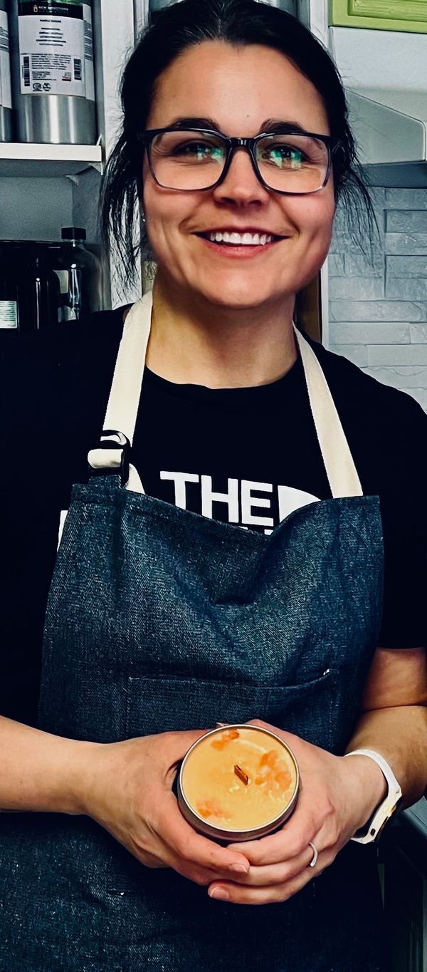 Smiling woman in apron holding a candle in a cozy kitchen.