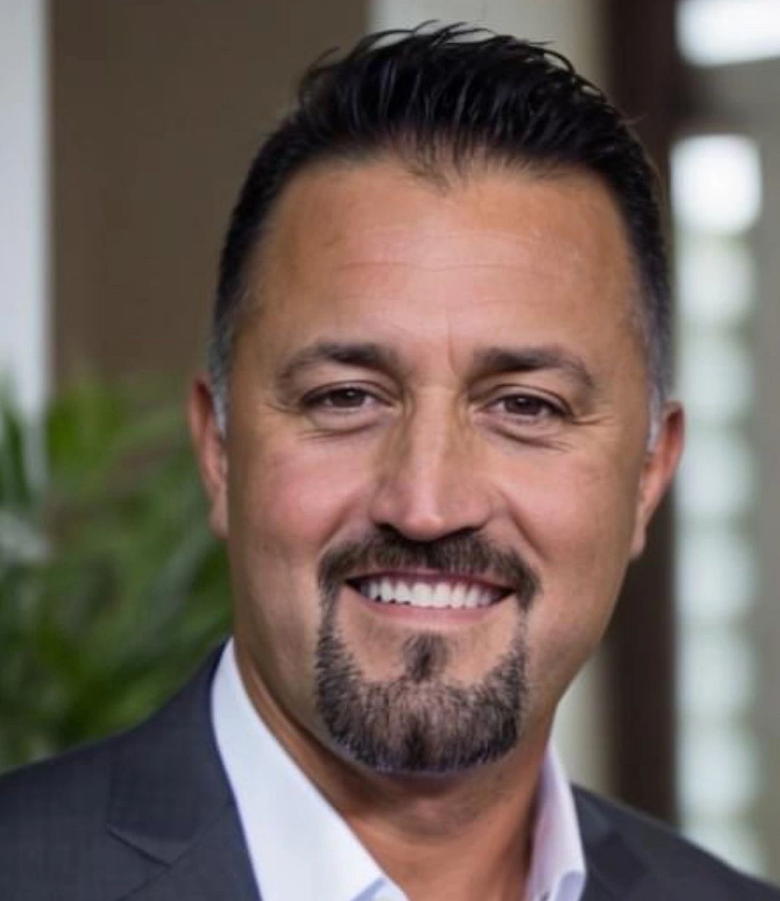 Smiling man with a goatee and dark hair in a suit jacket.
