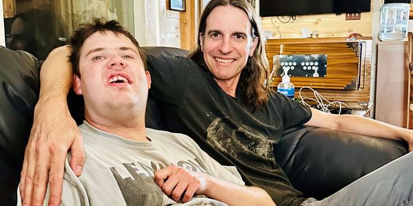 Two men sitting closely on a couch smiling.