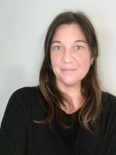 A woman with long brown hair wearing a black top smiles softly at the camera.