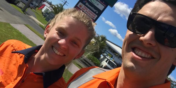 Two smiling workers in orange Coast Smart Electrical uniforms outside on a sunny day.