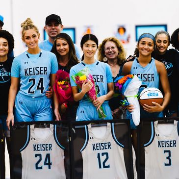 Keiser University women's basketball players celebrating with flowers and framed jerseys.