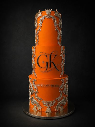 Tall orange cake with silver ornate designs.