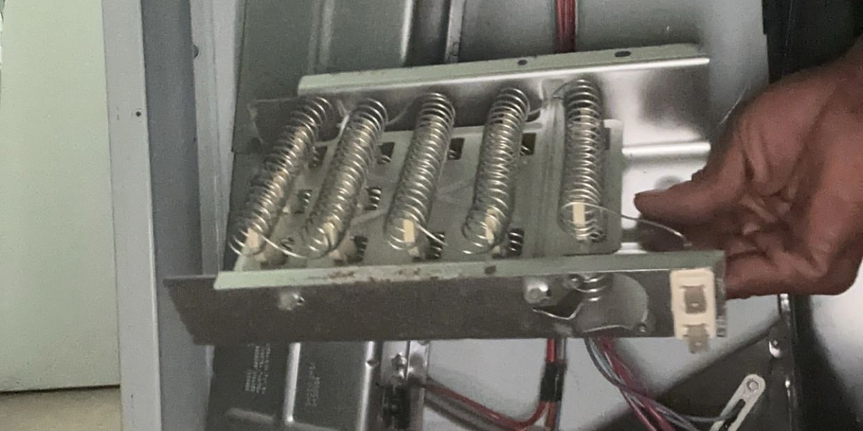 Hand holding a metal heating element with five coil springs inside a machine.