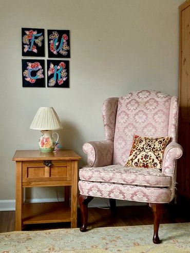 Cozy pink armchair with decorative pillow next to a wooden side table and lamp.