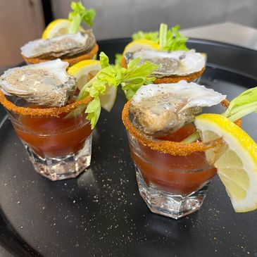 4 oyster shooters topped with shucked oyster, celery, lemon wedge and seasoning on the rim