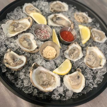 a dozen fresh shucked oysters on a tray over ice with cocktail sauce, lemon wedge and mignonette