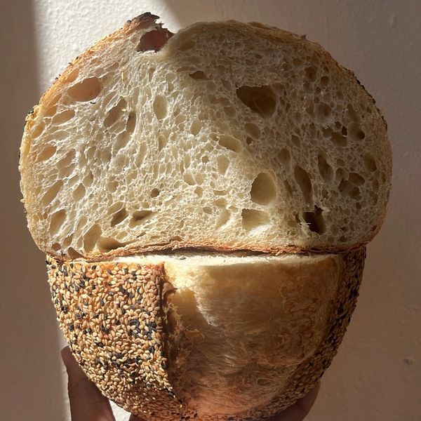Hand holding a sesame-seed crusted bread loaf cut in half.