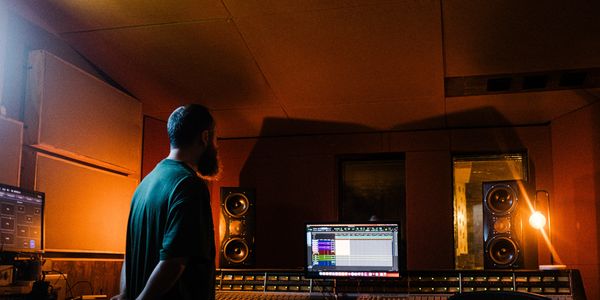 Callum Edwards standing at mixing console in orange-lit recording studio with large equipment