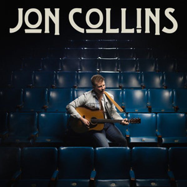 Jon Collins sits with acoustic guitar in empty theater with blue seats, name displayed above in whit