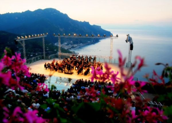Orchestra performing outdoors overlooking sea and mountains.