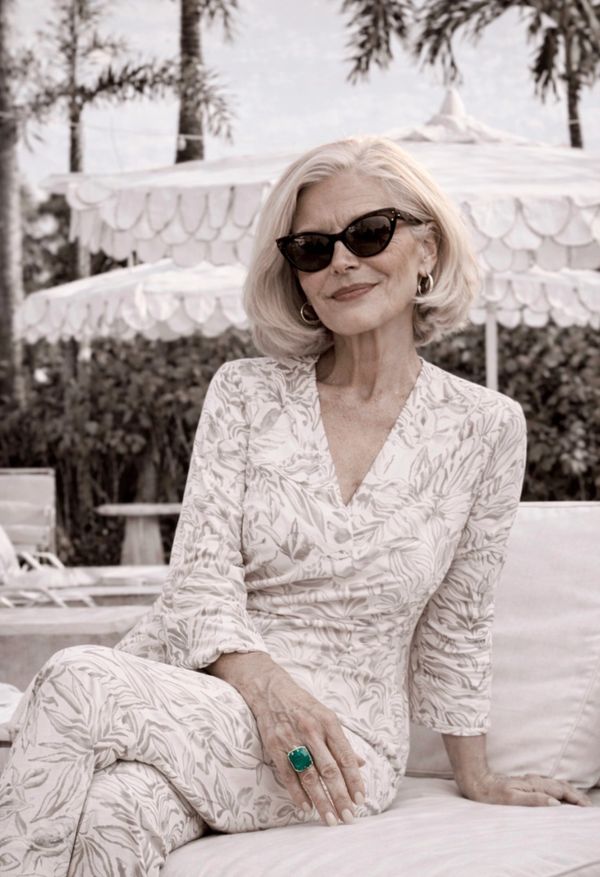 Elegant woman in floral dress and sunglasses relaxes outdoors.
