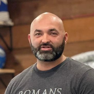 Bald man with a beard wearing a Romans shirt indoors.