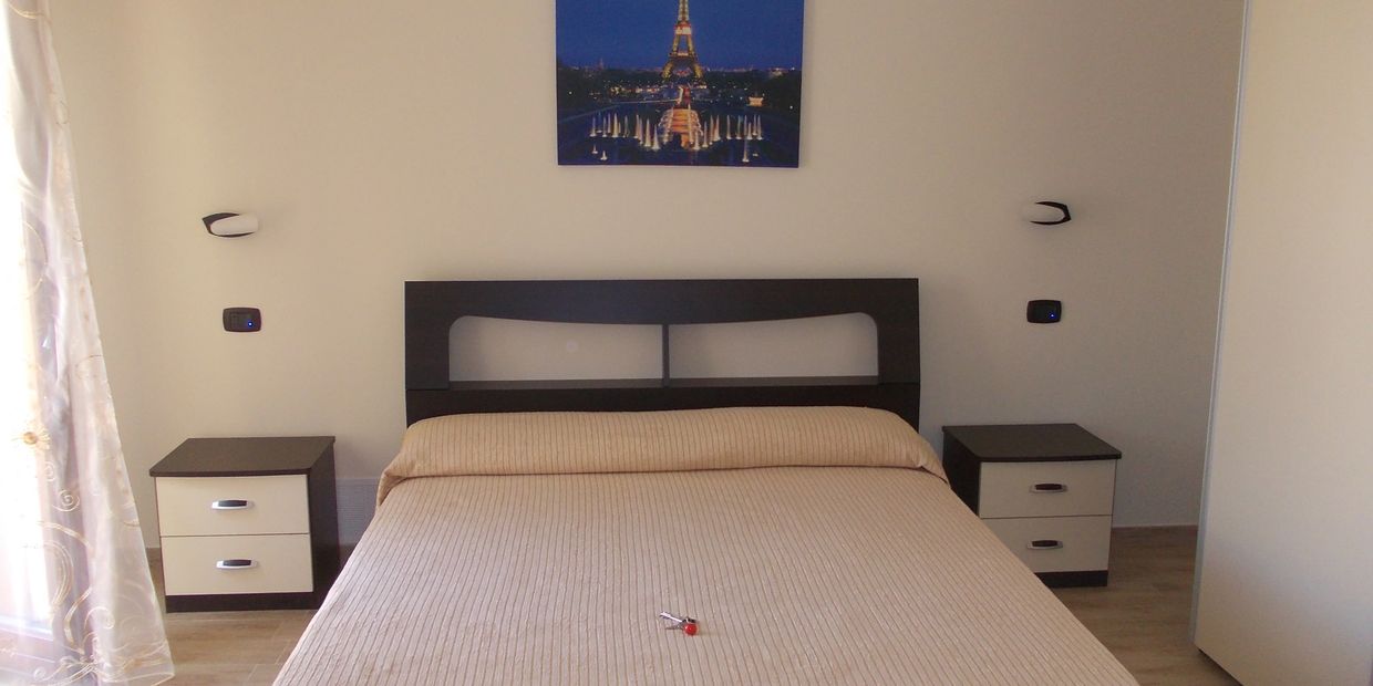 Minimalist bedroom with beige bedspread and Eiffel Tower artwork.