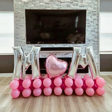 Decoración con globos rosados y plateados formando M y corazón.