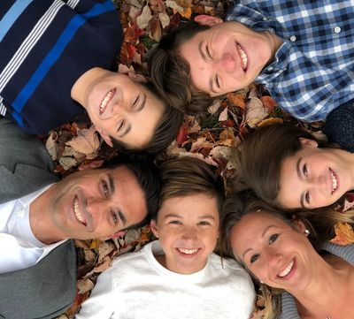 A smiling family lies in a circle on autumn leaves.
