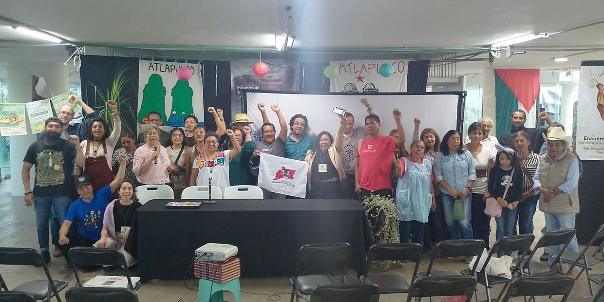 Group of people raising fists in solidarity at an indoor event with banners behind them.