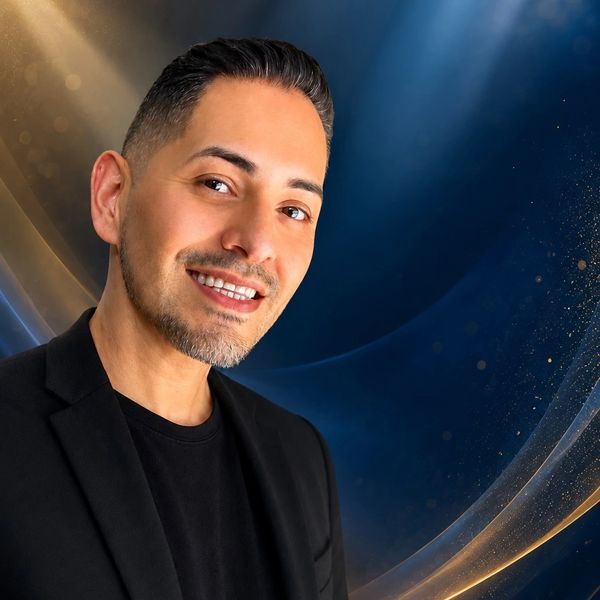 Smiling man in black jacket against a blue and gold abstract background.