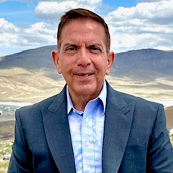 A man in a blue suit outdoors with mountains in the background.