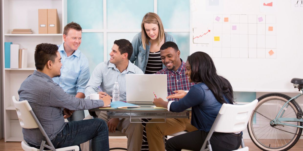 A diverse team collaborating around a laptop in a modern office.