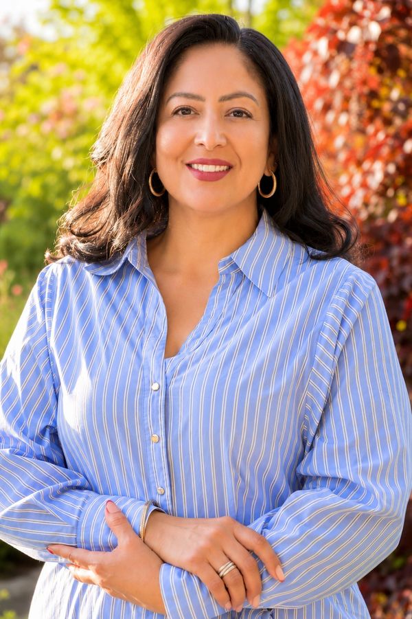 Smiling woman in a blue striped shirt outdoors with colorful foliage.