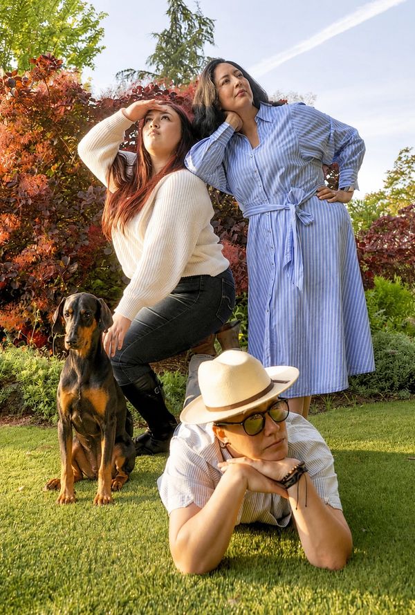 Three people and a dog posing outdoors on a sunny day, looking thoughtfully into the distance.