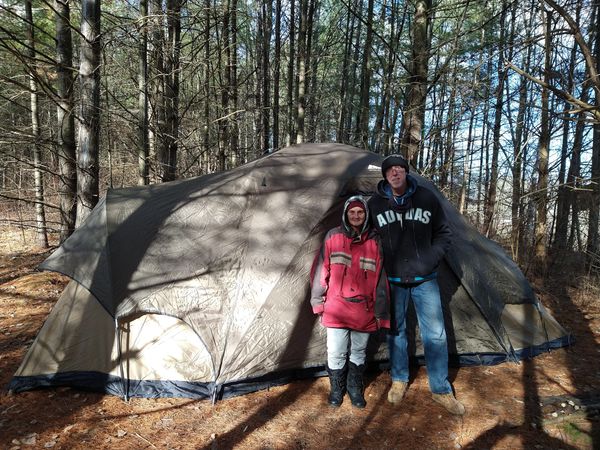 Two people standing in front of a large tent in a forest.