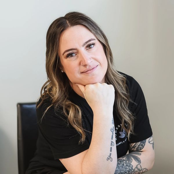 Woman with tattoos resting her chin on her hand, smiling gently.