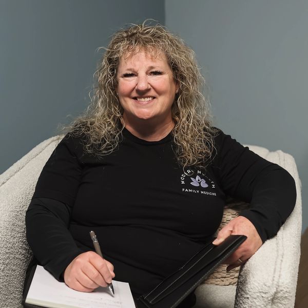 Smiling woman with curly hair writing in a notebook while sitting in a cozy chair.