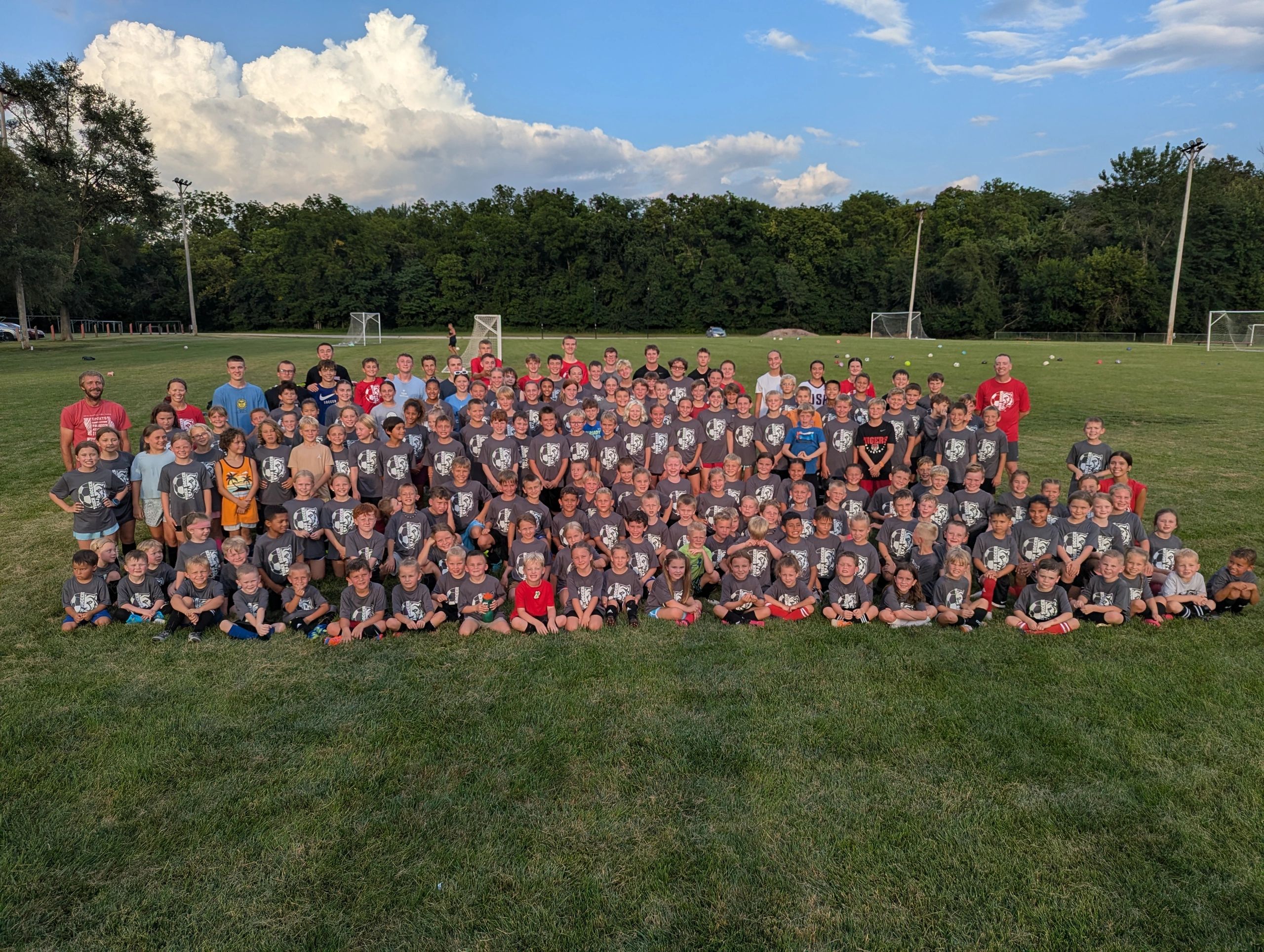 Large group of kids and adults posing on a soccer field.