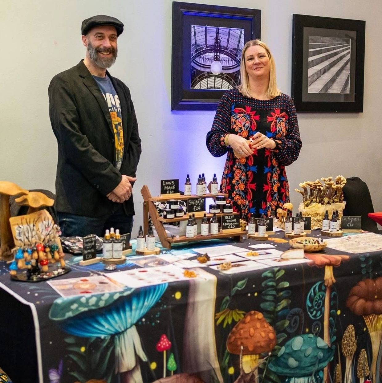Two people stand behind a colorful mushroom-themed product display table.