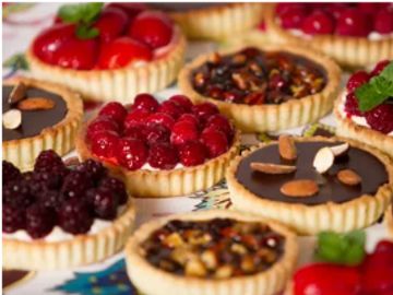 A colorful assortment of mini fruit and chocolate tarts, topped with berries, nuts, and mint.