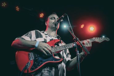 Musician performing on stage with a red guitar.