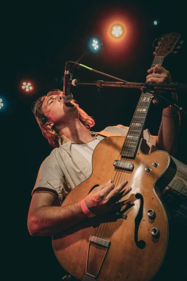 Musician passionately singing and playing guitar on stage.