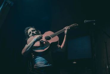 Musician passionately playing an acoustic guitar on stage.