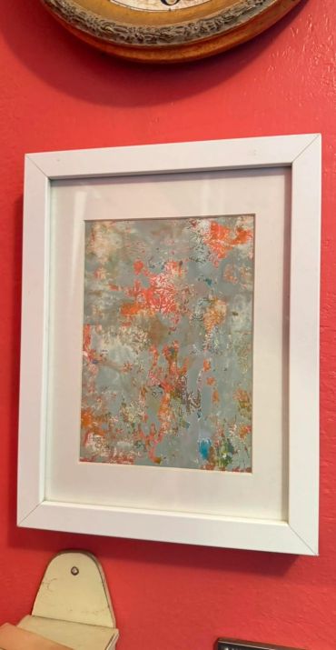 Abstract art in white frame on red wall.