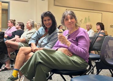 Two women sitting and smiling in a casual group setting indoors.