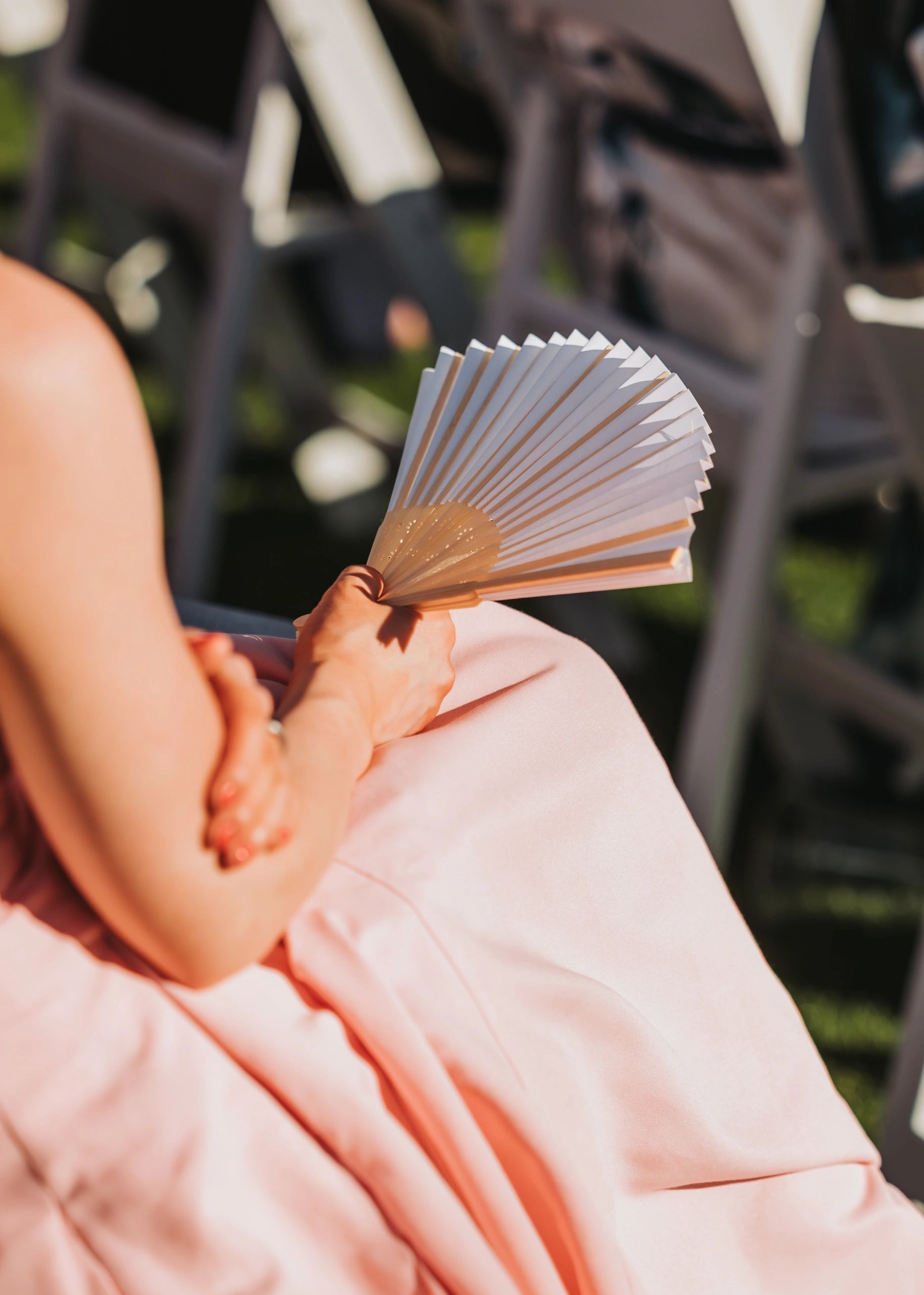 Person holding a white handheld fan wearing a pink dress.