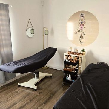 Minimalist massage or therapy room with two black-covered tables and a botanical wall art.