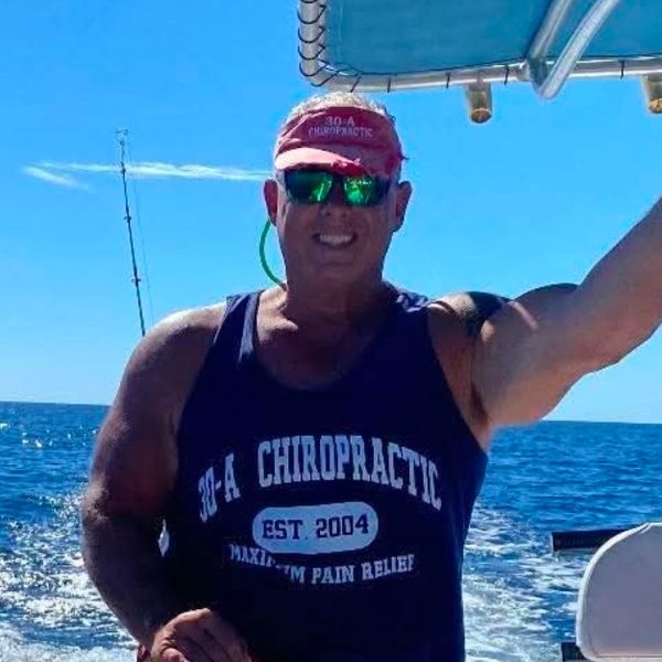 Man wearing a tank top and visor on a boat in the ocean.