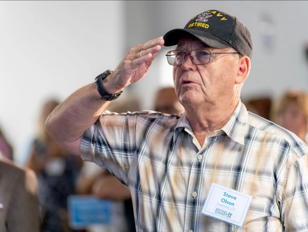 Steve saluting, wearing a Navy Retired cap and name tag.