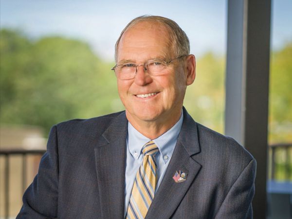 A headshot of Steve Olson in a suit and tie, sitting outside, smiling.